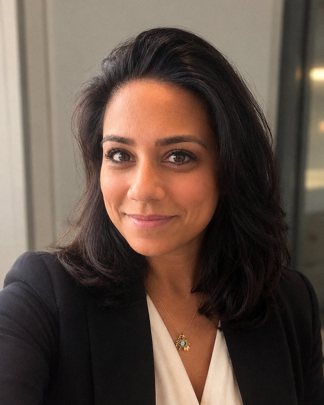 Natasha Seth, chest-up portrait, wearing a black blazer over a cream top, looking towards the camera.